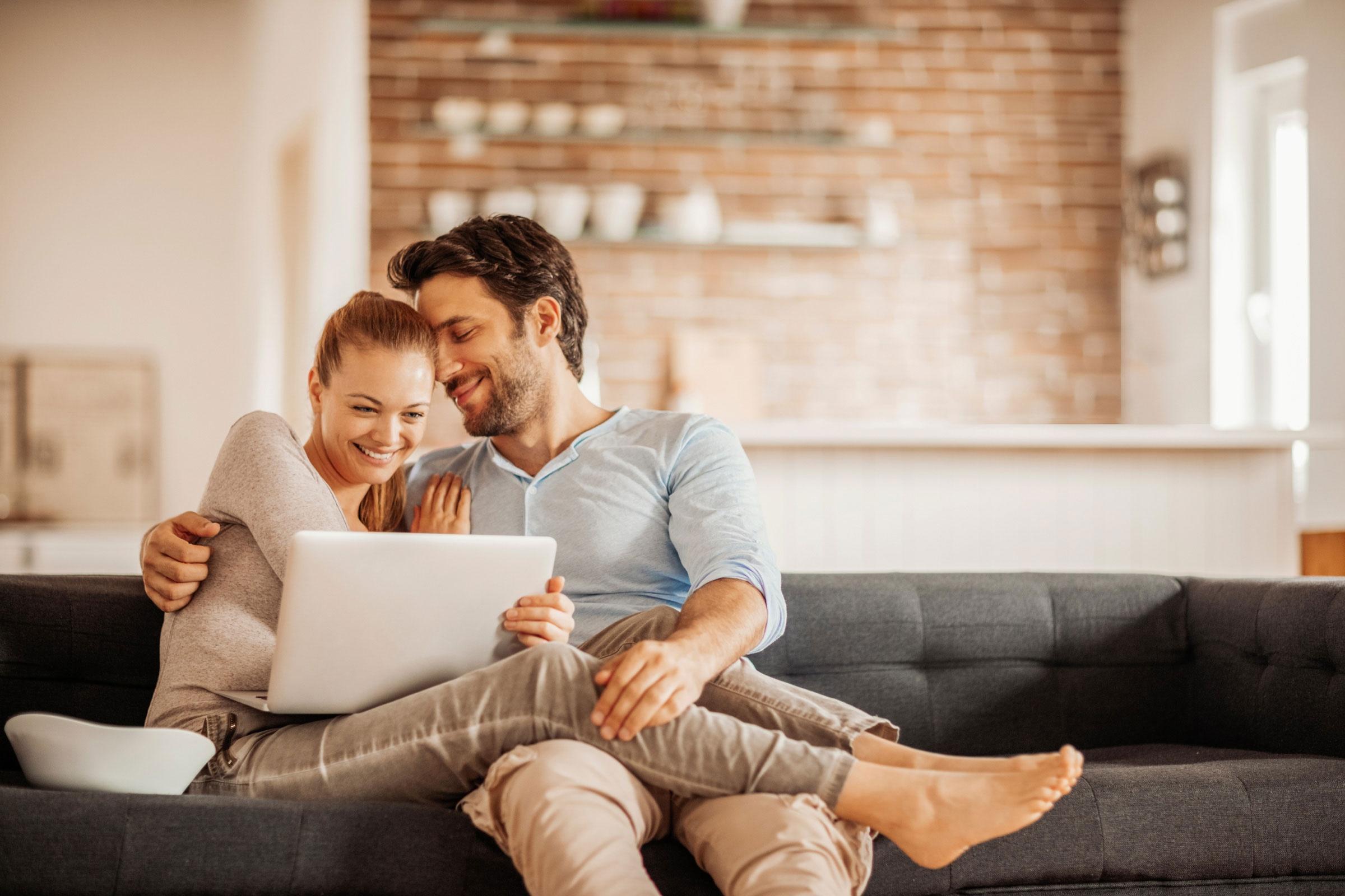 couple in pijamas hugging with laptop on couch