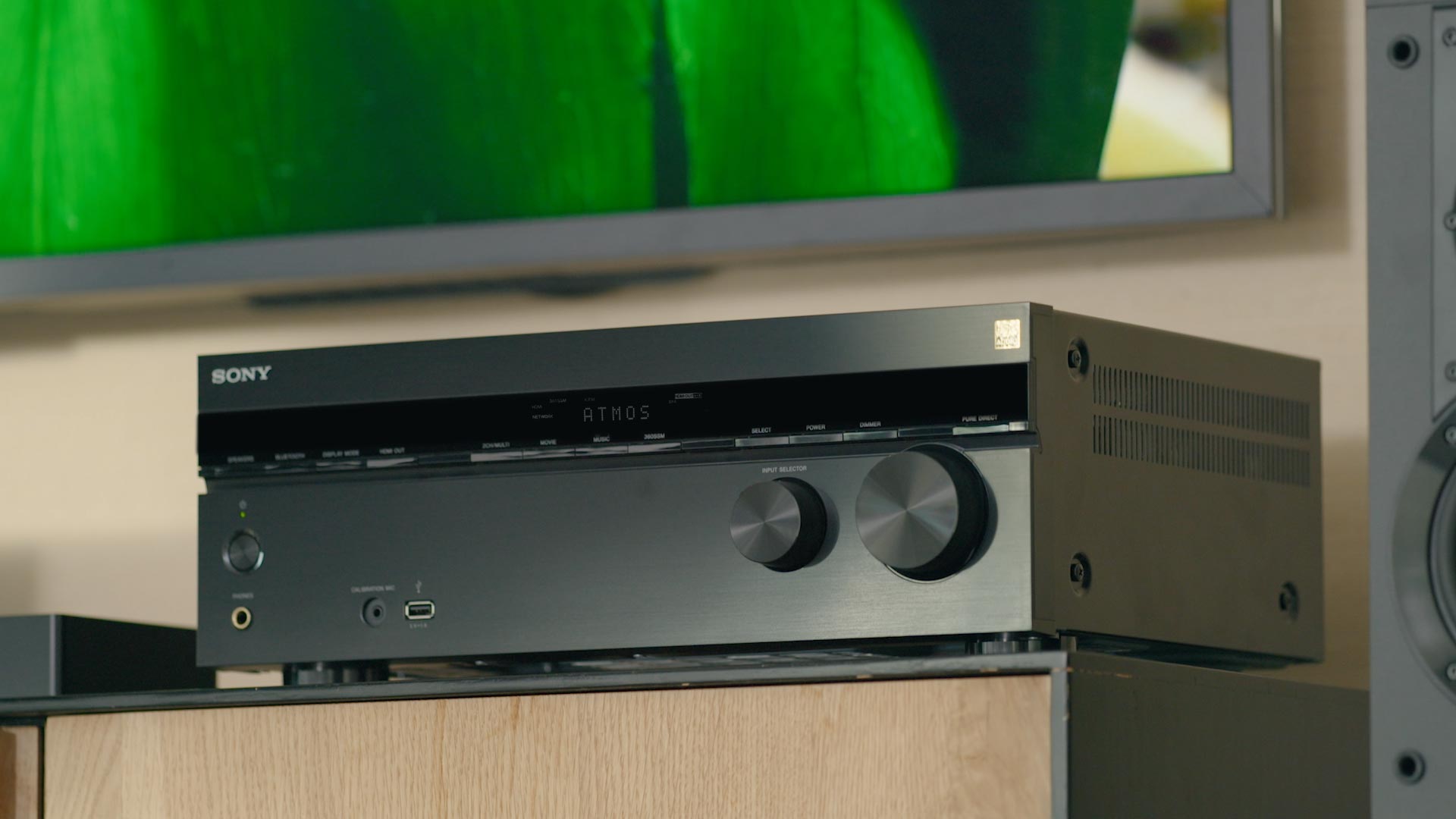 Sony Atmos receiver on wooden shelf below TV