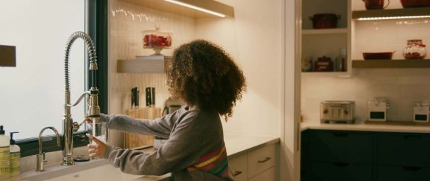 child filling up a cup of water in a nice kitchen with strip lighting